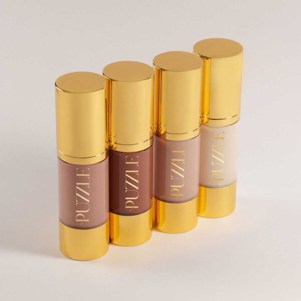 Four Puzzle Makeup Liquid Foundations with gold caps, displayed on a light gray background – vegan, skin-nourishing formula for natural coverage